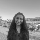 Black-and-white portrait of a smiling young woman with long hair on a coastal boardwalk